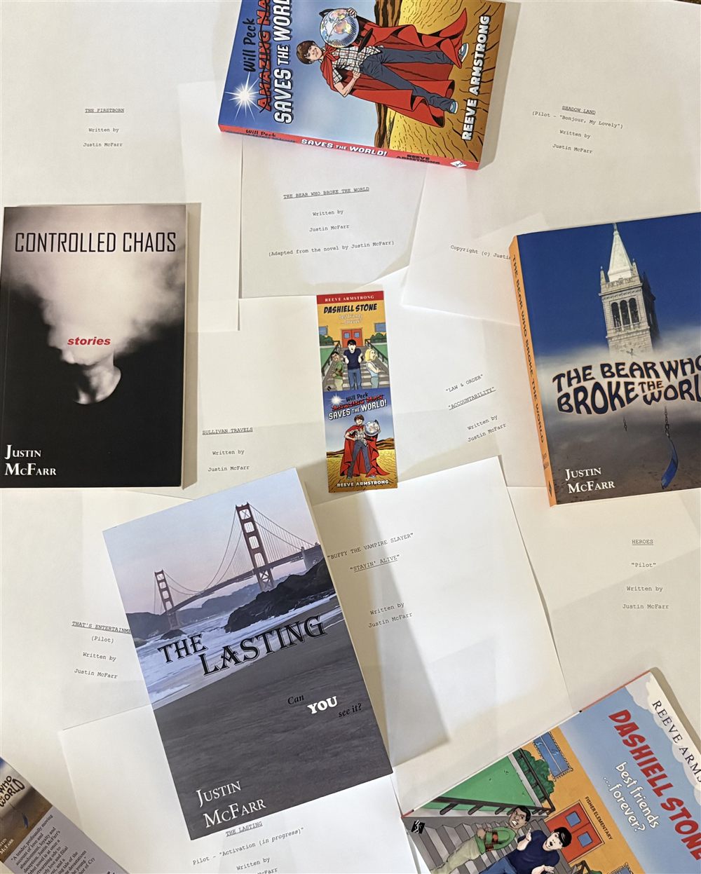 Justin McFarr's books and script title pages laid out together: The Bear Who Broke the World, Controlled Chaos, The Lasting, Will Peck Saves the World, Dashiell Stone, and screenplay title pages